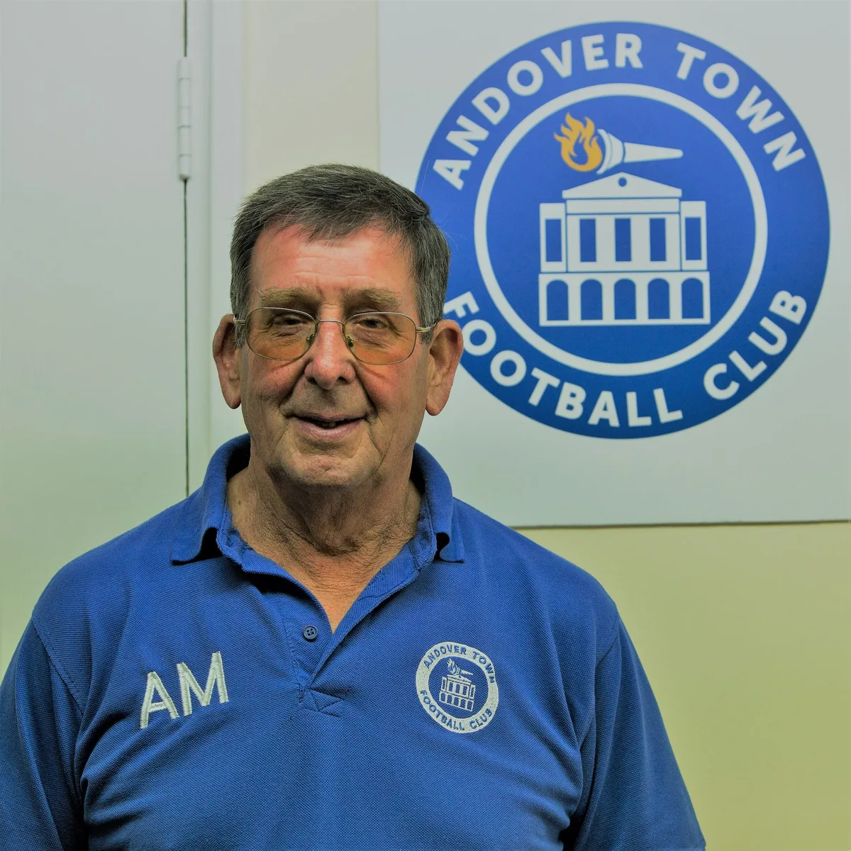 Alan Mussell in a blue Club shirt beside the Andover Town crest.