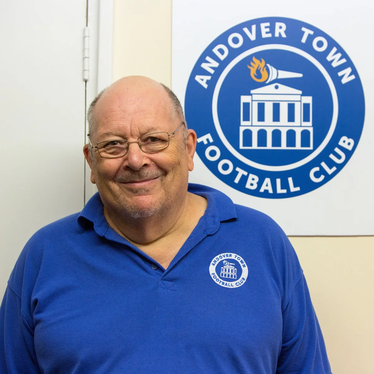 Graham Cousins in a blue Club shirt beside the Andover Town crest.